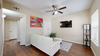 This single-floor residence offers a cohesive and functional layout designed for comfortable everyday living. The living room serves as the central gathering space, featuring rich hardwood-style flooring, neutral beige walls, and a ceiling fan with integrated lighting. A white sectional sofa anchors the room, complemented by a geometric-patterned area rug, a wall-mounted flat-screen TV, and a vibrant abstract wall painting that adds a bold pop of color to the otherwise understated palette.

An arched passageway connects the living and dining areas, lending an elegant architectural detail to the open flow. The dining area benefits from generous natural light through large windows fitted with horizontal blinds, accommodating a dark wood table surrounded by white chairs — ideal for meals and gatherings.

The kitchen is equipped with dark cabinetry, light countertops, a tile backsplash, and black appliances including a gas range, over-the-range microwave, and refrigerator — offering a practical and efficient cooking environment.

The two bedrooms are carpeted for comfort, each with neutral walls and window treatments that allow for natural light. The full bathroom features dark wood vanity cabinetry, a single-sink countertop, and a shower-tub combination, all laid over hardwood-style flooring that ties the space together cohesively.