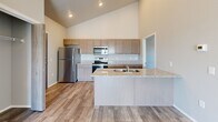 This well-designed two-bedroom, two-bathroom unit offers a thoughtfully planned single-level layout with notable architectural character. The open-concept living and kitchen area is anchored by dramatically vaulted ceilings that lend a sense of spaciousness well beyond the unit's compact footprint. An exposed cylindrical HVAC duct adds an industrial design accent overhead, complemented by a ceiling fan that enhances airflow throughout the main living space.

The kitchen features granite countertops, taupe shaker-style cabinetry, a stainless steel refrigerator, electric range, and microwave. A peninsula with an undermount double sink provides additional prep space and separates the kitchen from the living area. Wood-look plank flooring runs throughout the main living spaces, while the bedrooms are finished with plush carpet.

The living area opens directly to a private balcony through sliding glass doors, offering outdoor views and abundant natural light. Both bedrooms include windows that bring in additional daylight. The primary bedroom is a comfortable, well-proportioned size. One bathroom features a walk-in shower with built-in shelving nearby. Three closets provide practical storage throughout the unit.