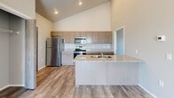 This well-designed two-bedroom, two-bathroom unit offers a thoughtfully planned single-level layout with notable architectural character. The open-concept living and kitchen area is anchored by dramatically vaulted ceilings that lend a sense of spaciousness well beyond the unit's compact footprint. An exposed cylindrical HVAC duct adds an industrial design accent overhead, complemented by a ceiling fan that enhances airflow throughout the main living space.

The kitchen features granite countertops, taupe shaker-style cabinetry, a stainless steel refrigerator, electric range, and microwave. A peninsula with an undermount double sink provides additional prep space and separates the kitchen from the living area. Wood-look plank flooring runs throughout the main living spaces, while the bedrooms are finished with plush carpet.

The living area opens directly to a private balcony through sliding glass doors, offering outdoor views and abundant natural light. Both bedrooms include windows that bring in additional daylight. The primary bedroom is a comfortable, well-proportioned size. One bathroom features a walk-in shower with built-in shelving nearby. Three closets provide practical storage throughout the unit.