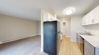 This compact yet efficiently designed one-bedroom, one-bathroom unit offers a thoughtful layout across a single floor. The galley-style kitchen is outfitted with white shaker cabinetry, white subway tile backsplash, light countertops, and black appliances including a refrigerator and electric range, complemented by a dishwasher and an under-mount sink. Light wood-look flooring runs throughout the kitchen and main living areas, adding warmth and continuity to the space. The living room is bright and open, featuring a large sliding glass door with vertical blinds that allows abundant natural light and provides outdoor access. A baseboard heating unit runs along the exterior wall. A connecting hallway leads to the bedroom and bathroom, keeping the layout functional and well-organized. The bedroom offers a comfortable footprint with soft carpeting, neutral walls, a ceiling fan with a light fixture, and a built-in sliding-door closet with shelving. The bathroom features a single-sink vanity with a white countertop, gray cabinetry, a framed mirror, and wood-look flooring. Textured ceilings are present throughout, and the overall color palette of soft neutrals creates a clean, calm ambiance throughout the unit.