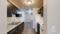 This single-floor unit offers a practical and comfortable layout with well-defined living spaces. The galley-style kitchen is a standout feature, showcasing dark espresso cabinetry with brushed nickel hardware, light granite-look countertops, a stainless steel double-basin sink, and a full suite of appliances including a refrigerator, dishwasher, and range. A flush-mount ceiling light illuminates the kitchen, which opens down a hallway toward the rest of the unit.

The living areas are finished with neutral-toned carpet and warm beige walls, creating a clean and inviting ambiance. Multiple rooms benefit from natural light through windows fitted with blinds, and a sliding glass door in one of the main rooms provides outdoor views and access to an exterior space, dressed with vertical blinds for privacy. Baseboard heaters are present throughout the carpeted rooms, and a wall-mounted air conditioning unit provides additional climate control.

The bathroom features a full tub-shower combo with a clean, white surround and chrome fixtures. The 3D floor plan reveals a well-organized layout with multiple rooms, a central hallway, and clearly defined functional zones, making this a thoughtfully arranged single-level space suited for comfortable everyday living.