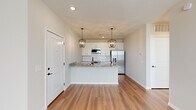 Located at 5060 Warner Rd in Westerville, Ohio, this thoughtfully designed single-floor residence combines modern finishes with a clean, neutral aesthetic throughout. The kitchen serves as the heart of the home, showcasing granite countertop surfaces, crisp white cabinetry, a decorative subway tile backsplash, and stainless steel appliances including a French door refrigerator. A central island with a built-in sink provides additional prep space and is illuminated by a pair of elegant cage-style pendant lights, creating a warm focal point in the open layout. Light wood-style flooring flows seamlessly through the main living and kitchen areas, enhancing the bright, airy feel of the space. The living area benefits from natural light through well-placed windows, lending an open and welcoming atmosphere. Bedrooms feature plush carpeting and access to outdoor areas via glass-paned doors. The primary suite connects directly to a well-appointed en-suite bathroom, complete with granite vanity counters, white cabinetry with matte black hardware, a glass-enclosed walk-in shower with white subway tile surround, and wood-look flooring. A generously sized walk-in closet with wire shelving provides ample storage. Additional rooms offer versatile, light-filled spaces suited to a variety of uses.