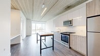 Located at 1590 Elmwood Ave in Evanston, IL, this modern one-bedroom, one-bathroom unit offers a thoughtfully designed layout with contemporary industrial-inspired finishes. Exposed concrete ceilings are a defining architectural feature throughout, complemented by light wood-tone flooring that runs seamlessly across the open-plan living and kitchen areas.

The kitchen is well-appointed with two-tone cabinetry — combining crisp white upper cabinets with wood-grain lower cabinets — stainless steel appliances including a gas range, built-in microwave, and refrigerator, plus a white subway tile backsplash. A freestanding island with a warm butcher block top and black steel frame serves as both a prep and dining area.

The living room is bathed in natural light, courtesy of expansive floor-to-ceiling sliding glass doors that frame sweeping views of the Evanston skyline and tree canopy. The bedroom is a comfortable, well-proportioned space with a window offering additional city views and an exposed concrete ceiling that carries the industrial aesthetic throughout.

The bathroom features large-format tile flooring, a wood-grain vanity with a white countertop, and a sliding glass door. A dedicated closet completes the unit, offering practical storage. The overall ambiance is clean, bright, and modern.