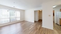 Located at 1100 Townsend Blvd in Fredericksburg, Virginia, this single-floor residence offers a well-organized and functional layout. The living area features warm wood-tone vinyl plank flooring, crisp white walls, and a ceiling fan, creating a bright and comfortable environment. Natural light filters in through windows fitted with blinds, enhancing the open feel of the space. The galley-style kitchen is efficiently designed with warm honey-toned wood cabinetry, granite-look countertops, a double-basin sink, and white appliances including a refrigerator, dishwasher, and electric range. A doorway at the end of the kitchen leads to additional storage or utility space. The bedrooms are finished with plush neutral carpeting and offer generous natural light through individual windows. At least one bedroom features a spacious walk-in closet with a full-width hanging rod, providing ample storage. The bathroom is well-appointed with a wood-cabinet vanity, white countertop, a full tub-shower combination, and matching vinyl plank flooring that ties the space together cohesively. Overall, the unit presents a clean, move-in-ready interior with a practical and comfortable design throughout.