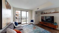 Located at 100 Commons Park North in Stamford, Connecticut, this contemporary residence offers a well-designed single-floor layout with an open and airy feel throughout. The living room serves as the centerpiece of the space, featuring rich hardwood-style flooring, large sliding glass doors that open to a private balcony, and sweeping views of the Stamford skyline. Natural light pours in through floor-to-ceiling windows, creating a bright and inviting atmosphere.

The kitchen is outfitted with stainless steel appliances, including a gas range, microwave, and full-size refrigerator, complemented by dark wood cabinetry, light countertops, and a large window that further enhances the sense of openness. A dedicated dining area adjoins the kitchen for convenient everyday living.

The bedrooms are generously sized, each benefiting from abundant natural light. The primary bedroom includes a built-in wall shelving unit and direct access to a walk-in closet and en-suite bath, while a secondary bedroom features expansive windows with elevated city views and a spacious closet. Both bathrooms are finished with neutral tones, white vanities, and tile flooring, offering a clean and functional design. The overall aesthetic is modern and cohesive throughout.