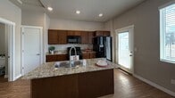 This 840-square-foot, two-story home on W Ecomeer Dr in Herriman, UT offers a practical and well-designed layout across two floors. The main level (320 sq ft) features an open-concept kitchen and living room with durable wood-style flooring and abundant natural light from large windows with blinds. The kitchen is equipped with rich dark-stained cabinetry, granite-style countertops, a kitchen island with a double-basin sink, and black appliances including a gas range, microwave, and refrigerator. A door off the kitchen provides exterior access. A half bathroom with a pedestal sink and mirror is also located on the main floor. The staircase leads to the upper level (520 sq ft), where the 130-square-foot primary bedroom features plush carpet, neutral grey walls, and windows that bring in natural light. A dedicated closet provides storage. The upper-level full bathroom includes a shower/tub combo with chrome fixtures. Throughout the home, neutral grey tones and white trim create a clean, cohesive aesthetic. Textured ceilings and recessed lighting add to the functional design of this efficiently laid-out Herriman residence.