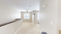 This single-floor unit offers a practical and cohesive layout designed for comfortable everyday living. The open living area is finished with neutral beige carpeting and features a ceiling fan, providing a light and airy atmosphere. Two windows along the far wall allow natural light to flow through the space while offering views of the surrounding neighborhood. A low half-wall with a dark wood cap rail defines the entry area, adding a subtle architectural detail.

The kitchen is well-equipped and functional, featuring rich dark-stained cabinetry, light granite-style countertops, and a full suite of stainless steel appliances, including a refrigerator, range, microwave, and dishwasher. Wood-look vinyl flooring runs throughout the kitchen, creating a clean transition from the carpeted living area. The sink is positioned along the lower cabinetry run, offering views into the adjoining living space.

The bathroom is neatly appointed with wood-look flooring, a full tub and shower combination with a curtain rod, a toilet, and a vanity with dark wood cabinetry. Additional overhead cabinetry provides practical storage. The overall palette throughout the unit remains consistently neutral, contributing to a clean and move-in-ready presentation.