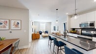 Located at 800 NW Ward Rd in Lee's Summit, MO, this well-appointed 2-bedroom, 2-bathroom residence offers a thoughtfully designed single-floor layout with modern finishes throughout. The open-concept living area seamlessly connects the kitchen, dining, and living spaces, all unified by light wood-look flooring and a neutral gray-toned palette. The kitchen is a standout feature, showcasing white cabinetry, dark subway tile backsplash, dark countertops, stainless steel appliances, and a central island with bar seating illuminated by globe pendant lights. The adjacent dining area provides an intimate space for meals, while the living room offers a comfortable, airy atmosphere with natural light streaming through large windows. The primary bedroom is a generously sized retreat with plush carpet, a large window with curtains, and ample closet space. The second bedroom mirrors the same calm aesthetic. Both bathrooms are finished with white vanities, black hardware accents, and wood-look flooring, with one featuring a full tub-shower combination. A dedicated laundry area with a full-size washer and dryer adds everyday convenience, completing this modern and functional Lee's Summit residence.