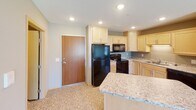 This single-floor unit is designed with a practical, comfortable layout that makes efficient use of its space. The kitchen serves as a functional hub, featuring light wood cabinetry, granite-style countertops, and a suite of black appliances including a refrigerator, electric range, and over-the-range microwave. A peninsula counter extends into the adjacent living area, creating a natural transition between spaces and offering additional prep or dining space. The entry door opens directly into this kitchen and living area, providing a welcoming and accessible flow throughout.

The bedrooms are carpeted and finished in neutral taupe tones, each featuring a window that allows natural light to filter in and offers views of the surrounding exterior. Baseboard heating runs along the perimeter walls, ensuring consistent warmth throughout the cooler months.

The unit includes two bathrooms, both featuring light wood vanities with white countertops and tile flooring. The full bathroom is equipped with a tub-shower combination and a large vanity mirror with overhead lighting. The second bathroom includes grab bars for added accessibility and safety, along with a single-sink vanity. Overall, the unit presents a clean, neutral aesthetic suited for a variety of living arrangements.
