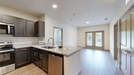 Located at 3300 Jupiter Road in Plano, Texas, this two-bedroom, one-bathroom residence offers a well-designed single-floor layout that maximizes functionality and comfort. The open-concept living area flows seamlessly from the kitchen, which serves as a central highlight of the home. Featuring dark espresso cabinetry, granite countertops, a peninsula with an undermount sink, and a full suite of stainless steel appliances — including a refrigerator, electric range, microwave, and dishwasher — the kitchen is both stylish and practical. Light wood-style flooring runs throughout the unit, complementing the neutral, bright white walls and creating a clean, cohesive aesthetic. The living area opens to a set of French doors that invite natural light and provide outdoor access. Both bedrooms are well-proportioned, with the primary bedroom offering generous square footage, a dedicated closet, and direct views of the surrounding greenery. The second bedroom also benefits from natural light through large windows. The bathroom is finished with large-format, marble-look tile surrounding a deep soaking tub, lending a refined touch. A hallway connects the key spaces efficiently, with two closets providing ample storage throughout the home.