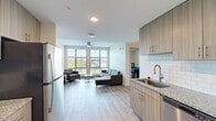 Located at 8700 Baltimore Ave in College Park, Maryland, this modern single-floor unit offers a well-designed open-concept layout with clean lines and contemporary finishes throughout. Light wood-look flooring flows seamlessly across the entire space, lending a cohesive and airy feel.

The kitchen is equipped with stainless steel appliances, including a refrigerator, electric range, and over-the-range microwave. Light wood cabinetry pairs with granite countertops and a classic white subway tile backsplash, while a stainless steel sink and dishwasher add to the functional design. The kitchen opens directly into the spacious living area, which is anchored by large floor-to-ceiling windows that invite abundant natural light and provide open outdoor views. A ceiling fan overhead enhances comfort in this bright, welcoming common space.

The bedroom is a comfortable, well-proportioned room featuring its own ceiling fan, light wood flooring, and a dedicated closet with built-in shelving for organized storage. The full bathroom offers a clean, modern aesthetic with white subway tile surrounding the bathtub and shower combination, light wood-look flooring, and recessed lighting. Additional cabinetry provides practical storage. The unit's modern design, quality finishes, and convenient College Park location make it a well-appointed and functional living space.