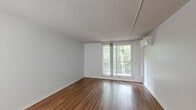 Located at 2900 Northwind Dr in East Lansing, Michigan, this studio unit offers an efficient, single-floor layout that makes smart use of its compact footprint. The open living area is finished with warm hardwood-style flooring that runs throughout, complemented by crisp white walls and a textured ceiling that add a clean, bright character to the space.

The integrated kitchen is positioned along one wall and is well-equipped with stainless steel appliances, including a refrigerator and an electric range, a built-in microwave, and a sink with ample white cabinetry above and below for storage. The open sightlines between the kitchen and living area create a sense of openness and ease of movement throughout the unit.

The living area benefits from a sliding glass door that opens to a private balcony, framing lush greenery views and allowing natural light to fill the room. A wall-mounted mini-split unit provides climate control.

The bathroom features full white tile surround in the shower and tub combo, a toilet, and clean, functional finishes throughout. A hallway with closet access connects the living space to the bathroom, offering practical storage solutions. Overall, this unit presents a straightforward, functional layout well-suited for single occupancy in the East Lansing area.
