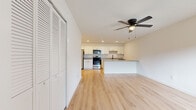 This single-floor unit offers a clean, modern aesthetic defined by a neutral white palette and light hardwood flooring that flows throughout the main living areas. The open-concept layout connects the living room to the kitchen seamlessly, creating a spacious and functional everyday living environment. The living area features a ceiling fan with a built-in light fixture, large windows that invite natural light, and a louvered bifold closet providing convenient storage.

The kitchen is well-appointed with white shaker-style cabinetry extending to the upper walls, offering generous storage capacity. Stainless steel appliances include a gas range, over-the-range microwave, refrigerator with French doors, and a sink with a matte black faucet set into a gray quartz-style countertop. A peninsula with a matching countertop defines the boundary between kitchen and living space, adding both prep area and a casual dining option.

The bedrooms feature plush neutral carpeting, ceiling fans, natural light from windows, and sliding or panel closets with wire shelving. A bathroom includes a white vanity with a marble-patterned countertop, an undermount sink, matte black fixtures, and light hardwood flooring, complementing the unit's cohesive design throughout.