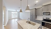 Located at 500 Dalton Way in Little River, South Carolina, this single-story, one-bedroom, one-bathroom home offers a thoughtfully designed open-concept layout. The combined kitchen and living area serves as the heart of the home, where light hardwood-style flooring, neutral gray walls, and recessed lighting create a bright, welcoming atmosphere. The kitchen is well-appointed with gray shaker-style cabinetry, granite countertops, a central island with an undermount sink, stylish pendant lighting, and a full suite of stainless steel appliances including a range, over-the-range microwave, and refrigerator. The living area extends naturally from the kitchen and features a ceiling fan and access to natural light through double doors. The bedroom is a comfortable retreat finished with plush carpeting, two windows with blinds, and a ceiling fan, providing a quiet and relaxing environment. The bathroom mirrors the home's refined aesthetic with granite countertops, gray cabinetry, a glass-enclosed shower, and hardwood-style flooring. A dedicated in-unit laundry room with wire shelving above accommodates a full-size washer and dryer. Additional features include a hallway, closet, and consistent, modern finishes throughout the entire home.