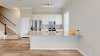 This two-story home in Montgomery, Texas offers a well-designed layout across both levels. The main floor showcases an open-concept living area with warm wood-look hardwood flooring, crown molding, and a ceiling fan overhead. A bank of large windows floods the living space with abundant natural light while providing views of the surrounding neighborhood. The kitchen is a standout feature, equipped with white cabinetry, granite countertops, a subway tile backsplash, stainless steel appliances, and a peninsula that serves as both a workspace and casual dining area. A staircase with classic balustrades connects the main floor to the upper level, where bedrooms are finished with plush carpet and ceiling fans. Each bedroom benefits from natural light through slatted blinds. The bathrooms are appointed with granite-topped white vanities, large-format tile flooring, and tub-shower combinations with full tile surrounds and brushed nickel fixtures. A convenient half bath is tucked under the staircase on the main level. Neutral tones throughout create a cohesive, move-in-ready atmosphere suited to a variety of interior styles.