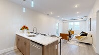 This well-designed 3-bedroom, 2-bathroom residence offers a thoughtfully laid-out single-floor plan that maximizes its footprint through clean lines and a contemporary aesthetic. The open-concept kitchen and living area serves as the heart of the home, featuring a large central island with a white quartz countertop, warm wood-toned cabinetry, stainless steel appliances including a refrigerator, range, and dishwasher, and stylish pendant lighting overhead. Light hardwood flooring flows seamlessly throughout, tying the spaces together. The living room benefits from natural light through large windows and a glass door that opens to a private balcony, creating a bright and airy ambiance. A stacked in-unit washer and dryer adds everyday convenience. Both bathrooms are finished with striking floor-to-ceiling marble-style wall surrounds and soaking tubs with chrome fixtures, lending a spa-like quality to the space. The three bedrooms are clean and understated, with neutral tones, hardwood flooring, and ample closet space. The primary bedroom offers a generous layout well-suited as a comfortable personal retreat. Throughout the unit, recessed lighting, white walls, and modern finishes create a cohesive, contemporary living environment.