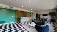 Located at 1262 N Fairfax Ave in West Hollywood, CA, the lobby of The Fitz on Fairfax makes a striking first impression with its bold black-and-white checkerboard tile flooring that flows throughout the entire space. The reception area anchors the lobby with a textured blue-green desk framed by warm vertical wood slat paneling set against a vibrant teal accent wall. An arched doorway adds an architectural flourish, leading further into the space where curated artwork punctuates the walls.

The lounge area is generously sized and furnished with plush emerald green and navy velvet seating, complemented by a round marble-top coffee table — creating a welcoming, stylish gathering spot. Large floor-to-ceiling windows along the street-facing wall flood this section with abundant natural light while offering open views of the neighborhood, and a gold-railed staircase adds an elegant vertical element.

A dedicated conference room features deep blue walls, a substantial marble conference table, leather chairs, wall-mounted display, and oval mirrors, providing a refined and functional meeting space. Additional areas include a mailroom wall lined with black mailboxes beneath a decorative textile wall installation, and an entry vestibule with eye-catching flamingo-print wallpaper and a tufted bench — together reflecting a cohesive, design-forward aesthetic throughout.