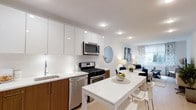 Located at 1133 Warburton Ave in Yonkers, NY, this one-bedroom, one-bathroom residence offers a thoughtfully designed single-floor layout with modern finishes and an open, airy feel. The kitchen is a standout feature, boasting sleek white cabinetry that extends to the ceiling, warm wood-toned lower cabinets, and stainless steel appliances including a gas range, built-in microwave, and dishwasher. A clean white countertop provides ample workspace and extends seamlessly into a dining area with a minimalist table and seating for multiple guests. Recessed lighting throughout ensures consistent, bright illumination. The open-concept design connects the kitchen and dining area directly to the living space, which is framed by a large window that invites generous natural light and features tasteful décor including a round accent mirror and a stylish sofa arrangement. The light-toned flooring throughout the main living area enhances the bright, contemporary ambiance. The overall design emphasizes clean lines, functional layout, and modern aesthetics, making this residence an attractive and well-appointed home in the Yonkers area.
