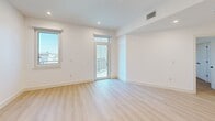 Located at 20 Medford St in Somerville, MA, this thoughtfully designed one-bedroom, one-bathroom residence offers a clean, modern aesthetic with high-quality finishes throughout. Light oak hardwood flooring runs continuously across the open-plan layout, complemented by crisp white walls and recessed lighting that create a bright, airy atmosphere.

The combined kitchen and living area serves as the heart of the home. The kitchen features a large waterfall-edge quartz island with an undermount sink and matte black faucet, warm wood cabinetry on the lower island, white upper cabinetry, stainless steel appliances including a range and built-in microwave, and stylish smoked glass pendant lights overhead.

The bedroom is a well-proportioned retreat bathed in natural light from multiple windows, with direct access to a private balcony offering outdoor views. The room includes a double-door closet with matte black hardware, and the unit additionally benefits from four closets total, providing exceptional storage.

The bathroom is finished in a contemporary style with large-format tile flooring, a wood-toned vanity with quartz countertop, matte black fixtures, and a glass-enclosed shower. An in-unit laundry room and a utility room add everyday convenience to this well-appointed Somerville residence.