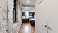 Located at 1821 E Hagert St in Philadelphia's vibrant Fishtown neighborhood, this one-bedroom, one-bathroom unit masterfully blends industrial character with modern finishes. The open-plan living and dining area flows seamlessly into a well-appointed kitchen, where exposed brick walls, original hardwood floors, and visible overhead piping pay homage to the building's industrial heritage. Tall, arched multi-pane windows flood the space with abundant natural light while reinforcing the historic architectural aesthetic.

The kitchen is a standout feature, equipped with rich dark-toned cabinetry, a central island with a built-in sink and white countertops, and a full suite of stainless steel appliances including a refrigerator, range, and microwave. Exposed wooden ceiling beams add warmth and texture overhead.

The bedroom offers a comfortable, private retreat with hardwood flooring, clean white walls, and convenient access to a closet. The bathroom is finished in a clean, contemporary style, featuring large-format gray tile throughout, a soaking tub with a tiled shower surround, and a modern vanity. In-unit laundry adds to the overall convenience of this thoughtfully designed space.