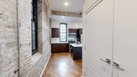 Located at 1821 E Hagert St in Philadelphia's vibrant Fishtown neighborhood, this one-bedroom, one-bathroom unit masterfully blends industrial character with modern finishes. The open-plan living and dining area flows seamlessly into a well-appointed kitchen, where exposed brick walls, original hardwood floors, and visible overhead piping pay homage to the building's industrial heritage. Tall, arched multi-pane windows flood the space with abundant natural light while reinforcing the historic architectural aesthetic.

The kitchen is a standout feature, equipped with rich dark-toned cabinetry, a central island with a built-in sink and white countertops, and a full suite of stainless steel appliances including a refrigerator, range, and microwave. Exposed wooden ceiling beams add warmth and texture overhead.

The bedroom offers a comfortable, private retreat with hardwood flooring, clean white walls, and convenient access to a closet. The bathroom is finished in a clean, contemporary style, featuring large-format gray tile throughout, a soaking tub with a tiled shower surround, and a modern vanity. In-unit laundry adds to the overall convenience of this thoughtfully designed space.