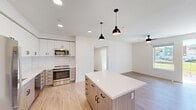 This well-designed single-floor residence offers three bedrooms and three bathrooms with a clean, contemporary aesthetic throughout. The open-concept kitchen serves as the heart of the home, featuring a central island with a white quartz countertop, two-tone cabinetry combining crisp white upper cabinets with warm wood-toned lower cabinets, a classic subway tile backsplash, and a full suite of stainless steel appliances including a refrigerator, range, microwave, and dishwasher. Stylish matte black pendant lights hang above the island, complementing the recessed lighting and a ceiling fan in the adjoining living area. Light-toned hardwood-style flooring runs seamlessly throughout, enhancing the bright, airy feel of the space. The primary bedroom offers a comfortable footprint with a wall-mounted mini-split system for individualized climate control and a sliding-door closet with built-in shelving. Additional bedrooms are equally well-appointed with natural light from large windows. The bathrooms are finished with wood-grain vanity cabinetry, white countertops, and matte black fixtures, with at least one featuring a full soaking tub and shower combination. A dedicated hallway connects the rooms efficiently, and two entrances provide added convenience and accessibility.