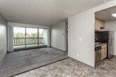 This single-floor unit offers a practical and functional layout across several well-defined spaces. The living area is generously proportioned, featuring plush carpeting, a ceiling fan, and a textured ceiling. A full-width sliding glass door fills the room with natural light and opens directly onto a private balcony, which overlooks a landscaped outdoor setting with tree views—particularly striking during autumn foliage season.

The galley-style kitchen is efficiently designed with light wood cabinetry lining both walls, granite-look countertops, and a drop-panel ceiling with integrated lighting. Stainless steel appliances, including a refrigerator and dishwasher, are complemented by a black electric range, and the stone-tile flooring adds a durable, neutral finish throughout the kitchen and entryway areas.

The bedroom is carpeted and includes a ceiling fan, built-in wire shelving for storage, and a window that provides additional natural light. A separate open room with drop-panel ceiling and dual flooring surfaces offers flexible use as a secondary living or recreational space.

The bathroom is clean and well-appointed, featuring a light wood vanity with a white countertop, a mirrored medicine cabinet, a tub-shower combination, and matching stone-tile flooring consistent with the rest of the unit.