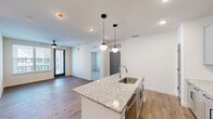 This well-appointed 2-bedroom, 2-bathroom residence is thoughtfully designed on a single floor, offering a clean, modern aesthetic with quality finishes throughout. The open-concept layout connects the kitchen and living area seamlessly, creating an inviting and functional living space. The kitchen serves as the heart of the home, anchored by a granite-topped island with a built-in sink and pendant globe lighting above. Gray shaker-style cabinetry, a marble-look tile backsplash, stainless steel appliances, and warm hardwood-style flooring complete the contemporary look. The living area extends naturally from the kitchen, featuring a ceiling fan and access to an outdoor balcony through a glass-panel door, allowing for ample natural light and outdoor views. The primary bedroom is generously sized, finished with plush carpet, a ceiling fan, and direct access to its own en-suite bathroom. The second bedroom also features carpet flooring and large windows that invite natural light. Both bathrooms are finished with elegant marble-look tile surrounds — one featuring a walk-in glass shower and the other a full soaking tub. Stylish gray interior doors add a cohesive, modern touch throughout the space, tying together the home's refined design sensibility.