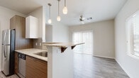 This well-appointed single-floor residence showcases a clean, contemporary design with a cohesive neutral palette and quality finishes throughout. The heart of the home is an open-concept kitchen and living area, where the kitchen features granite countertops, a tile backsplash, warm wood-toned lower cabinetry, crisp white upper cabinets, and stainless steel appliances. A peninsula with an overhanging countertop provides casual bar seating, while elegant pendant lighting adds a stylish focal point above. The living area flows seamlessly from the kitchen, highlighted by wood-look flooring, a ceiling fan, and a large sliding glass door with vertical blinds that allows abundant natural light to fill the space. The bedroom offers plush wall-to-wall carpeting, a ceiling fan, and a bright window with exterior views, creating a comfortable and restful retreat. Two bathrooms serve the residence — one featuring a soaking tub and shower combination with full tile surround, a wood-grain vanity, and wood-look flooring; the other a half-bath with a modern floating vanity, white countertop, and large mirror. A dedicated laundry area with hookups and dryer venting rounds out the functional layout of this thoughtfully designed home.