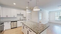 Located at 1 Hatcher Drive in Stockbridge, GA, this thoughtfully designed 2-bedroom, 1-bathroom single-story home offers a clean, modern aesthetic throughout. Light wood-tone flooring flows seamlessly across all rooms, complementing the crisp white walls and bright, airy atmosphere.

The open-concept kitchen and living area serves as the heart of the home. The kitchen is well-appointed with white shaker-style cabinetry, granite countertops, a herringbone tile backsplash, stainless steel appliances, and a central island with pendant lighting above — ideal for both cooking and entertaining. The adjoining living room is spacious and open, with recessed lighting and a large window that brings in natural light.

Both bedrooms are comfortably sized with light-filled windows offering outdoor views and durable wood-tone flooring. The primary bedroom includes a ceiling fan and generous proportions. A dedicated walk-in closet features built-in wire shelving systems for organized storage.

The full bathroom is well-designed with white cabinetry, granite countertops, a large mirror with lighting, and a full tub-shower combo with clean tile surround. The entrance provides a welcoming transition into the home. Throughout, the consistent use of neutral tones and modern hardware creates a cohesive, move-in-ready living environment.