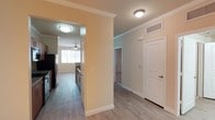 This single-floor residential unit is part of a well-maintained multi-story stucco complex, characterized by its southwestern-style architecture with neutral earth tones and balconies. The exterior features mature desert landscaping, shaded parking, and attached garages, contributing to a welcoming curb appeal.

Inside, the unit showcases a practical and comfortable layout finished with light wood-style flooring throughout, crisp white crown molding, and warm neutral wall tones. The kitchen is equipped with stainless steel appliances and offers a streamlined, efficient workspace. Adjacent to the kitchen, a central hallway connects the main living areas, with smooth transitions between rooms facilitated by clean architectural archways.

The living area benefits from a ceiling fan and a window that invites natural light, creating a bright and airy atmosphere. The entry area features a classic paneled white door with a thermostat nearby, highlighting the unit's practical design considerations. Flush-mount ceiling fixtures provide consistent overhead lighting throughout.

The layout flows logically, with additional rooms accessible from the main corridor, offering versatile spaces suitable for various uses. Overhead HVAC venting ensures year-round climate comfort. Overall, the unit combines functional design with clean finishes, making it a well-organized and comfortable living space.