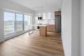 Located on the 15th floor at 131 Mill Street in Toronto's vibrant Distillery District neighbourhood, this one-bedroom, one-bathroom unit offers a thoughtfully designed layout with a clean, modern aesthetic throughout. Light hardwood flooring runs continuously across the entire space, complementing the crisp white walls and creating a bright, cohesive feel.

The open-concept kitchen is a standout feature, showcasing white upper cabinetry paired with warm natural wood lower cabinets and a matching central island with a white quartz countertop. Stainless steel appliances, including a refrigerator, built-in microwave, and range, complete the well-appointed cooking space. Floor-to-ceiling windows flood the kitchen with natural light and frame impressive city views.

The bedroom is a calm, minimalist retreat featuring large corner windows that capture sweeping views of the Toronto skyline and surrounding cityscape. Sleek floor-to-ceiling sliding panel closets provide ample storage while maintaining the room's clean lines.

The bathroom is finished with large-format tile flooring, a wall-mounted white basin vanity, warm wood cabinetry, and a framed mirror, delivering a spa-like simplicity. Throughout the unit, the consistent use of natural wood tones, white surfaces, and abundant natural light creates a refined, contemporary ambiance ideal for modern urban living.