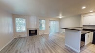 Located at 11305 SE Kent Kangley Rd in Kent, Washington, this two-story residence offers a well-designed layout spread across two levels. The main living area is open and airy, featuring light hardwood-style flooring, a tile-surround fireplace, and multiple windows with vertical blinds that invite abundant natural light. Sliding glass door access connects the living space to the outdoors, enhancing the sense of openness. A half-wall peninsula separates the living and dining areas from the kitchen, which is outfitted with white shaker-style cabinetry, dark granite countertops, and black appliances including a range, microwave, and refrigerator. An in-unit laundry area is conveniently accessible directly from the kitchen. The dining area features the same hardwood-style flooring and baseboard heating found throughout the main level. Bedrooms are carpeted and receive generous natural light through vertical-blind-covered windows, each equipped with baseboard heating for year-round comfort. Bathrooms are finished with wood-look flooring, white vanity cabinetry, dark granite countertops, and a full tub-shower combination. The overall aesthetic is clean and modern, with a neutral color palette throughout both floors.