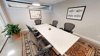 This 250 square foot conference room, located at 150 Broad Street in Windsor, CT, exemplifies modern professional design. The space is characterized by its clean lines and contemporary aesthetic. A large white conference table dominates the room, surrounded by ergonomic mesh chairs that provide comfort for extended meetings. Overhead, circular pendant lights offer ample illumination, complemented by natural light from transom windows.

The room's most striking feature is its extensive use of glass walls, creating a sense of openness and connectivity with the surrounding office space. These transparent barriers maintain privacy while fostering a collaborative atmosphere. The polished concrete floors are partially covered by a vibrant area rug, adding warmth and acoustic dampening to the space.

Wall-mounted artwork and strategically placed plants contribute to a refined yet inviting ambiance. Modern amenities include a wall-mounted television for presentations and climate control for optimal comfort. The room's design seamlessly blends functionality with style, making it an ideal setting for important business discussions, client meetings, or team collaborations in a professional environment.