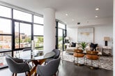 This contemporary urban residence is defined by its expansive floor-to-ceiling windows that frame sweeping city views and flood every room with natural light. The open-concept living and dining area is anchored by structural columns and rich hardwood flooring, creating a sophisticated yet welcoming atmosphere. Large black-framed windows wrap the corner of the living space, offering panoramic sightlines over the surrounding cityscape.

The kitchen is thoughtfully designed with light wood cabinetry extending from floor to ceiling, a marble-style backsplash, white quartz countertops, a gas cooktop, and stainless steel Bosch wall oven and microwave — providing both style and high-end functionality. The seamless cabinetry and clean lines give the kitchen a refined, contemporary character.

The primary bedroom features a full wall of floor-to-ceiling windows overlooking the city, while the secondary bedroom also benefits from natural light and hardwood flooring. Both rooms offer a calm, restful ambiance. The bathroom is finished with tile surround, a modern wood vanity, backlit mirror, and clean, neutral tones.

Overall, this residence presents a polished modern aesthetic with high-quality finishes, generous natural light, and impressive elevated city views throughout.