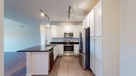 Located at 500 S Third St in Geneva, IL, this single-floor residence offers a clean, modern aesthetic throughout its thoughtfully designed layout. The kitchen is a standout feature, showcasing crisp white shaker-style cabinetry that extends to the ceiling for generous storage, complemented by dark countertops, a classic subway tile backsplash, and a full suite of stainless steel appliances including a range, over-the-range microwave, refrigerator, and dishwasher. Wood-look flooring and track lighting complete the kitchen's polished look. The bedroom areas are finished with plush wall-to-wall carpeting and feature notably tall ceilings that lend an open, airy feel. One bedroom benefits from a ceiling fan and a window with shutters that allows natural light to filter in. The bathroom is finished with tile flooring, a granite-topped vanity with white cabinetry, a large mirror, and a glass-enclosed shower. A dedicated utility and laundry room houses a full-size washer and dryer alongside the water heater and HVAC system, providing convenient all-in-one functionality. The overall ambiance of the space is bright, neutral, and move-in ready.