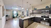 Located at 11901 S Freedom Park Dr in Herriman, Utah, this well-appointed single-floor residence combines modern design with functional living. The open-concept layout seamlessly connects the kitchen, dining, and living areas, creating a bright and airy atmosphere enhanced by light wood-tone flooring and neutral wall tones throughout.

The kitchen is a standout feature, equipped with dark espresso cabinetry, white quartz countertops, stainless steel appliances including a range, microwave, dishwasher, and refrigerator, and a central island with pendant lighting overhead. The island also provides casual bar seating, making it an ideal hub for both cooking and entertaining.

The living and dining area benefits from generous natural light through large windows dressed with elegant drapes, vaulted ceilings with track lighting, and ample space for comfortable furnishings.

The two bedrooms are carpeted for warmth and comfort, each featuring large windows, ceiling fans, and generous storage. The primary bedroom offers a relaxed, restful ambiance with room for substantial furniture.

The bathroom is finished with light tile flooring, white cabinetry with a rich wood-toned countertop, and a backlit vanity mirror, conveying a clean and polished aesthetic. An in-unit laundry area adds everyday convenience to this thoughtfully designed residence.