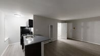 This studio unit in Milwaukee, Wisconsin offers a practical and well-designed single-floor layout suited for efficient urban living. The open main living area is finished with durable hardwood-style plank flooring in a warm gray tone and neutral gray walls, creating a clean, modern aesthetic throughout. A window along one wall allows natural light to fill the space, enhancing its open feel.

The kitchen is positioned along one side of the main room and features a peninsula-style countertop with a dark finish, providing a natural division between the living and cooking areas. Dark-finish cabinetry with a gas range, range hood, and black refrigerator complete the kitchen, offering a cohesive and functional cooking space.

A wall-mounted heating unit is centrally located within the main room, and interior doors lead to a closet and the unit's entry. The bathroom is finished with light-toned vinyl flooring, a white vanity with an integrated sink and framed mirror, and bright overhead lighting, keeping the space clean and functional.

Overall, this studio presents a straightforward, move-in-ready layout with consistent modern finishes, making it a practical option in the Milwaukee, WI 53233 area.