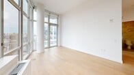 Located at 1 Ocean Dr in Brooklyn's Coney Island neighborhood, this modern one-bedroom, one-bathroom residence offers a thoughtfully designed layout bathed in natural light. Light-toned hardwood flooring runs throughout, complementing the clean white walls and contemporary aesthetic.

The open-plan kitchen and living area serves as the heart of the home. The kitchen is outfitted with sleek, high-gloss white cabinetry, a textured tile backsplash, stainless steel appliances — including a refrigerator, oven, and dishwasher — and an undermount sink. Floor-to-ceiling windows in the living area flood the space with daylight and frame expansive views of the Brooklyn skyline and surrounding neighborhoods.

The bedroom is a well-proportioned retreat featuring large windows that capture city views and allow generous natural light. It includes access to multiple closets, providing ample storage. A private balcony accessible from the living area extends the living space outdoors with additional panoramic views.

The bathroom is finished with striking floor-to-ceiling marble-style wall tiles, warm beige stone floor tiles, a wood-toned vanity with an undermount sink, and a full bathtub with shower. An in-unit laundry area and a hallway with additional closets round out the practical features of this well-appointed residence.