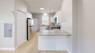 Located at 33-35 Rowe Ave in Hartford, CT, this single-floor, two-bedroom, two-bathroom unit offers a thoughtfully designed layout that maximizes its compact footprint. Light gray walls, light-toned hardwood flooring, and white trim create a clean, cohesive aesthetic throughout.

The kitchen is a standout feature, equipped with stainless steel appliances including a range, microwave, dishwasher, and refrigerator. White shaker-style cabinetry pairs with granite countertops and an L-shaped peninsula that provides additional prep and serving space. A window above the sink brings in natural light.

Both bedrooms feature wall-mounted mini-split HVAC units for individual climate control, light hardwood floors, and windows fitted with blinds. The primary bedroom includes dual closets—one a standard hinged-door closet and one a sliding-door closet—offering generous storage. The second bedroom is bright and well-proportioned.

The two bathrooms are distinctly finished. One features marble-style wall tile with a mosaic-tiled shower floor and darker floor tile, while the second presents a warmer palette with cream tile and a terracotta accent band in the shower. Both include walk-in showers and clean, modern fixtures.