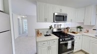 This well-appointed 2-bedroom, 1-bathroom single-floor residence offers a thoughtfully designed layout that balances comfort and functionality. The kitchen serves as a central highlight, featuring crisp white cabinetry with raised-panel doors and brushed nickel hardware, complemented by bright white countertops that enhance the sense of cleanliness and space. Stainless steel appliances, including a gas range and an over-the-range microwave, add a modern, polished touch. The kitchen flows openly into the adjoining living area, which is finished with light-toned carpeting that creates a warm and cohesive atmosphere throughout. Neutral white walls and flush-mount lighting keep the interiors feeling bright and airy. The open sightline from the kitchen through to the hallway and beyond provides a natural sense of depth and connectivity between the rooms. Decorative copper accents add a subtle warmth and personality to the kitchen space. The overall design aesthetic is clean and contemporary, with a neutral palette that offers a versatile canvas for personalization. This residence is well-suited for those seeking a move-in-ready home with practical, modern finishes in a comfortable, single-level setting.