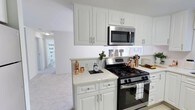 This well-appointed 2-bedroom, 1-bathroom single-floor residence offers a thoughtfully designed layout that balances comfort and functionality. The kitchen serves as a central highlight, featuring crisp white cabinetry with raised-panel doors and brushed nickel hardware, complemented by bright white countertops that enhance the sense of cleanliness and space. Stainless steel appliances, including a gas range and an over-the-range microwave, add a modern, polished touch. The kitchen flows openly into the adjoining living area, which is finished with light-toned carpeting that creates a warm and cohesive atmosphere throughout. Neutral white walls and flush-mount lighting keep the interiors feeling bright and airy. The open sightline from the kitchen through to the hallway and beyond provides a natural sense of depth and connectivity between the rooms. Decorative copper accents add a subtle warmth and personality to the kitchen space. The overall design aesthetic is clean and contemporary, with a neutral palette that offers a versatile canvas for personalization. This residence is well-suited for those seeking a move-in-ready home with practical, modern finishes in a comfortable, single-level setting.