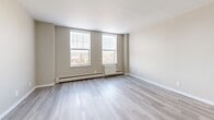 Located at 265 College St in New Haven, CT, this one-bedroom, one-bathroom unit offers a well-organized and efficiently designed layout across a single floor. Light wood-style flooring runs throughout the space, lending a clean, cohesive aesthetic complemented by neutral warm-gray walls and crisp white trim.

The combined kitchen and living area forms the heart of the unit. The kitchen is outfitted with white cabinetry featuring modern hardware, dark quartz-style countertops, a stainless steel sink, and stainless steel appliances including an electric range and built-in microwave — providing a functional and contemporary cooking space. The adjacent living area is open and bright, benefiting from natural light and a comfortable sense of scale.

The spacious primary bedroom is a standout feature, accommodating generous room for furniture arrangement. Large windows allow ample natural light and offer views of the surrounding New Haven cityscape, while baseboard heating units ensure year-round comfort. A dedicated closet with built-in shelving and a hanging rod provides practical storage.

The bathroom is finished with clean white subway tile surrounding a tub-shower combination with chrome fixtures, paired with a dark-topped vanity and an undermount sink, creating a polished and functional space. The overall design of the unit reflects modern, move-in-ready finishes throughout.