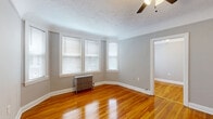 Located at 9907 Lake Rd in Cleveland's 44102 neighborhood, this single-floor, 3-bedroom, 1-bathroom residence offers a practical and well-appointed layout. Gleaming hardwood floors run throughout the bedrooms and hallway, catching natural light and lending warmth to the neutral gray-painted walls. The spacious primary bedroom is a standout feature, with a angled bay-style window arrangement, a ceiling fan with light fixture, a classic cast-iron radiator, and a textured ceiling. The two additional bedrooms are well-proportioned, each with hardwood floors, ceiling fans, natural window light, and cast-iron radiators. The bedrooms are served by five closets in total, providing generous storage throughout. The kitchen is equipped with warm wood cabinetry, dark countertops, a white gas range, tile backsplash, and resilient flooring. The bathroom is finished in crisp white with a full tub-shower combo, a mosaic tile floor, a pedestal sink, and a glass block window that provides privacy while allowing diffused natural light. Clean white trim and consistent gray-toned walls unify the home's interior, creating a cohesive and move-in-ready aesthetic throughout.