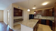 This single-floor residence offers a thoughtfully designed layout that balances functionality with comfort. The kitchen serves as a central highlight, showcasing rich dark cherry cabinetry, granite countertops, a central island with pendant lighting, a textured stone tile backsplash, and black appliances including a range, microwave, and refrigerator. A built-in granite-topped counter nook provides additional workspace or casual dining space.

The open living and dining area features warm hardwood-style flooring, a ceiling fan, and a chandelier that adds a touch of elegance. Large glass doors flood the living space with natural light and provide views to the outdoors, creating a bright and welcoming atmosphere.

The bedrooms are finished with plush carpeting, ceiling fans, and windows fitted with blinds that let in generous amounts of natural light while maintaining privacy. Outdoor views can be glimpsed through the windows, adding a sense of openness to each room.

Both bathrooms are finished with tile flooring and dark-countered vanities with rich wood cabinetry. One bathroom features a tub and shower combination, while the other offers a walk-in shower, both equipped with accessibility grab bars. Light tile flooring ties each bathroom together with a clean, cohesive look throughout the home.