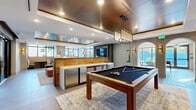 Located in Miami, FL, this well-appointed fitness center offers a spacious, single-floor layout designed to accommodate a full spectrum of workout needs. The space is defined by its open, airy design, with floor-to-ceiling windows and large glass doors lining multiple walls, flooding the interior with abundant natural light and providing views of the surrounding greenery and outdoor areas.

The cardio zone is comprehensively equipped with treadmills, elliptical machines, Assault fitness runners, and stationary cycling bikes featuring interactive screens. A dedicated strength training area houses a full dumbbell rack, an Octagon functional training rig, battle ropes, a heavy punching bag, and plyo boxes, supporting both high-intensity and traditional resistance training. Full-length mirrors along one wall enhance the sense of space and allow for form monitoring during workouts.

The flooring throughout combines light-toned, textured fitness flooring with rubber mat zones beneath equipment, ensuring both safety and durability. Ceiling fans provide additional ventilation, complementing the bright, recessed lighting overhead. A refreshment station with a mini-refrigerator and storage is tucked into one corner, adding convenience. Large glass doors open directly to an outdoor turf area, seamlessly extending the workout experience beyond the walls of the facility.