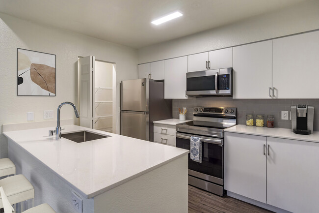 Renovated Package I kitchen with stainless steel appliances, cream quartz countertops, white cabinetry, grey tile backsplash, and hard surface flooring. - Avalon at Bear Creek