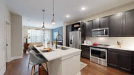 This 1-bedroom, 1-bathroom residence offers a thoughtfully designed single-floor layout that maximizes every square foot. The open-concept kitchen and living area serves as the heart of the home, anchored by a striking white quartz waterfall island with seating, dark espresso cabinetry, and a full suite of stainless steel appliances including a French door refrigerator, electric range, microwave, and dishwasher. Stylish pendant lighting and rich hardwood-style flooring add warmth and character to the space. The living room is bright and inviting, featuring large windows dressed with sheer curtains that flood the room with natural light, complemented by a bold accent wall in a deep slate blue and a modern multi-bulb chandelier. The bedroom offers a comfortable, carpeted retreat with a ceiling fan, natural light from a window with blinds, and a warm accent wall. The full bathroom is well-appointed with dark wood double vanities, white quartz countertops, matte black hardware, hardwood-style flooring, and direct access to a dedicated walk-in closet. A stacked in-unit washer and dryer is also included. The layout flows efficiently, connecting all rooms with clean sightlines and consistent design details throughout.