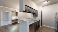 Located at 6300 SW Rutland Rd in Bentonville, Arkansas, this single-story residence offers a well-designed layout with contemporary finishes throughout. The galley-style kitchen is a standout feature, showcasing dark espresso cabinetry, granite countertops, and a full suite of stainless steel appliances including a refrigerator, electric range, built-in microwave, and dishwasher. A peninsula with a granite overhang provides a convenient pass-through to the open living area, which features wood-look flooring and crown molding. The living space flows seamlessly toward the entryway, creating an airy and connected feel. The bedrooms are generously sized, finished with plush carpeting, ceiling fans, and windows that invite natural light. Each bedroom offers access to walk-in closets equipped with wire shelving for ample storage. The bathrooms are finished with granite vanities, dark cabinetry with brushed nickel hardware, wood-look flooring, and tiled tub-shower combinations. A dedicated in-unit laundry area accommodates a full-size washer and dryer. The overall aesthetic is clean and modern, with a neutral color palette that complements the rich cabinetry and stone surfaces throughout.