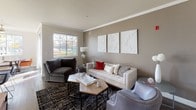 This single-floor residence offers a thoughtfully designed layout with a range of well-finished living spaces. The living room is a welcoming centerpiece, featuring warm neutral tones, crown molding, wood-style flooring, and ample natural light streaming through large windows. The kitchen is outfitted with dark espresso cabinetry, stainless steel appliances including a refrigerator, range, and microwave, complemented by granite-style countertops and wood-style flooring for a sleek, modern aesthetic. The dining area is positioned near a large picture window that frames outdoor greenery, and includes a ceiling fan overhead, creating a bright and comfortable space for meals. Multiple bedrooms provide comfortable retreats, each featuring plush carpeting, crown molding, and ceiling fans. One bedroom showcases a bold accent wall and a walk-in closet, while another offers direct outdoor access through a glass door alongside a wall-mounted television and a multi-drawer dresser. The bathrooms are clean and functional, featuring tub and shower combinations with curved curtain rods, granite-style vanity countertops, dark wood cabinetry, and wood-style tile flooring. Overall, the space combines modern finishes with a neutral, versatile palette to create a comfortable and cohesive living environment.